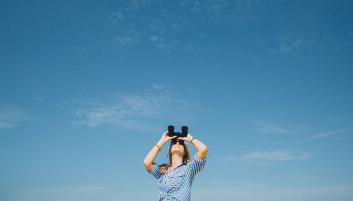 woman looking through binoculars up at the sky