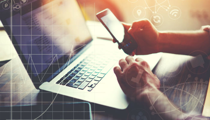 man sitting at laptop with mobile phone in hand
