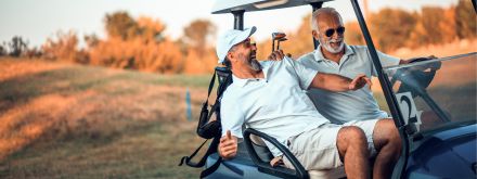 Two men in a golf buggy on a sunny golf course, laughing together