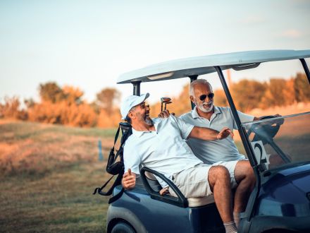 Two men in a golf buggy on a sunny golf course, laughing together