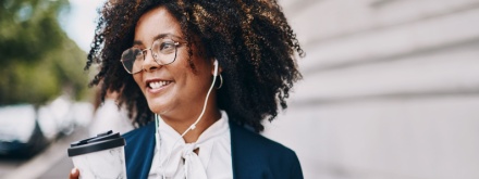 business woman with headphones in walking with coffee in hand