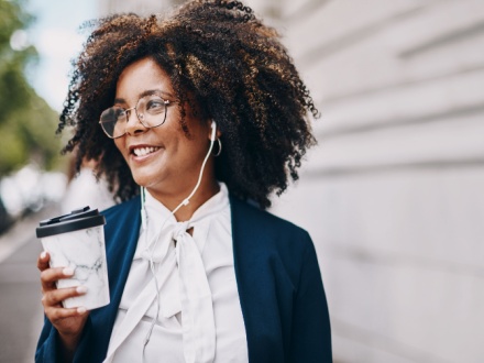 business woman with headphones in walking with coffee in hand