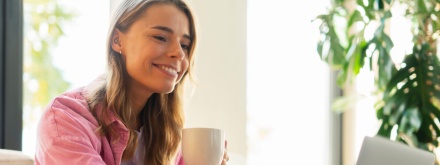 smiling woman having coffee at her laptop