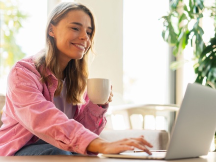 smiling woman having coffee at her laptop
