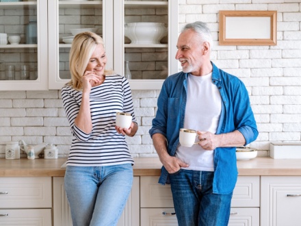 Mature woman and man spending time together standing at home kitchen drink tea