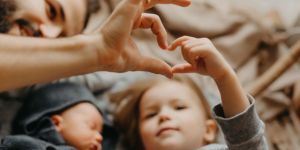 An adult and a child create a heart shape together with their hands, while a baby lies nearby, symbolizing love and family connection.