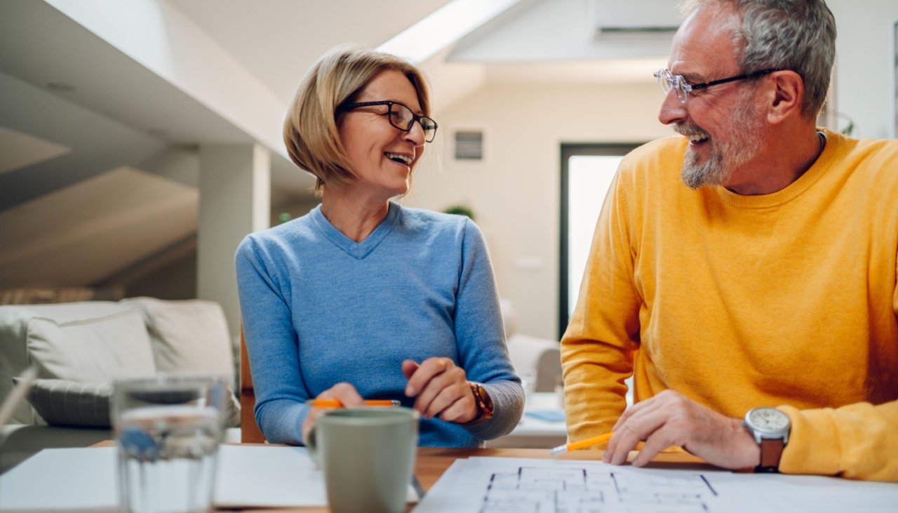 Elderly senior couple sitting at table while working on a blueprints of their new home