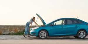 young woman looking under the hood of her broken car