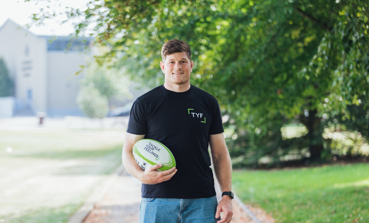 Rugby player Jack O’Donoghue holding a rugby ball with Tackle your feelings written on it