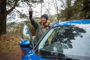 Woman at blue car waving