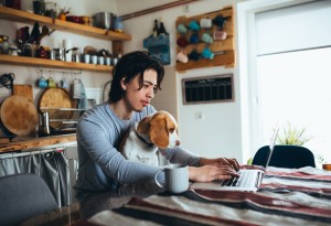 man at kitchen table on laptop with dog