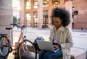 woman on laptop outside with bike