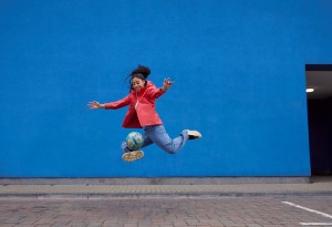 young girl playing football against blue wall